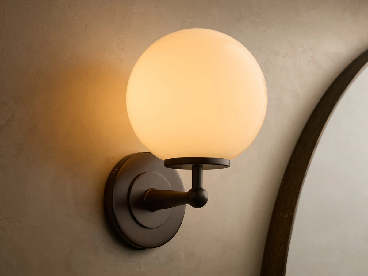 Fulton antique bronze wall sconce illuminated with a spherical milk glass globe