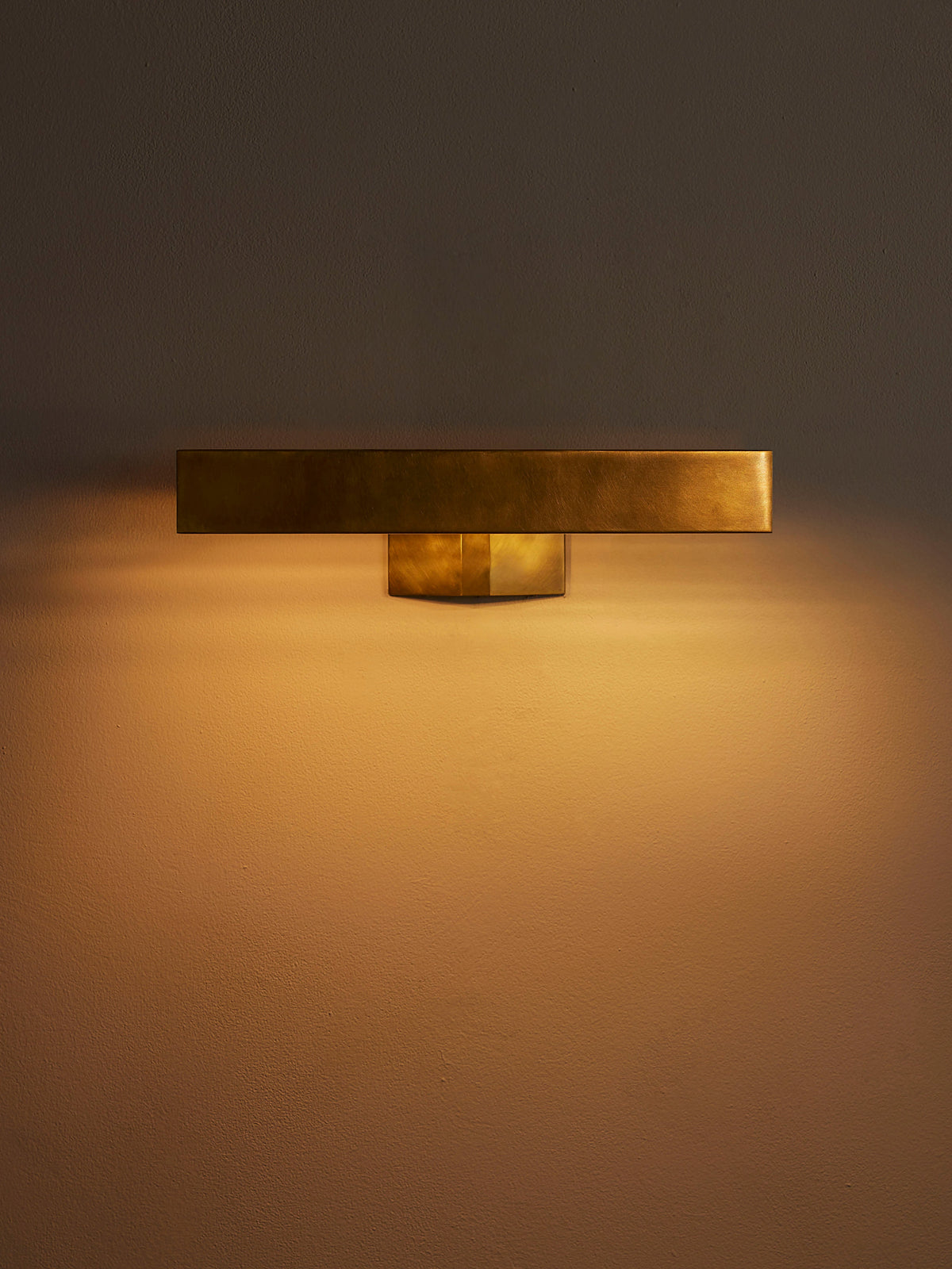Enrica brass picture light illuminated against a neutral wall