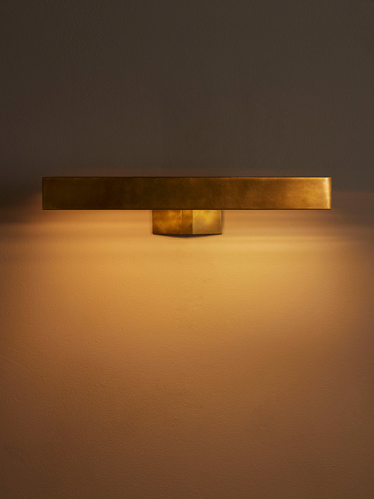 Enrica 18-inch brass picture light illuminated against a neutral wall