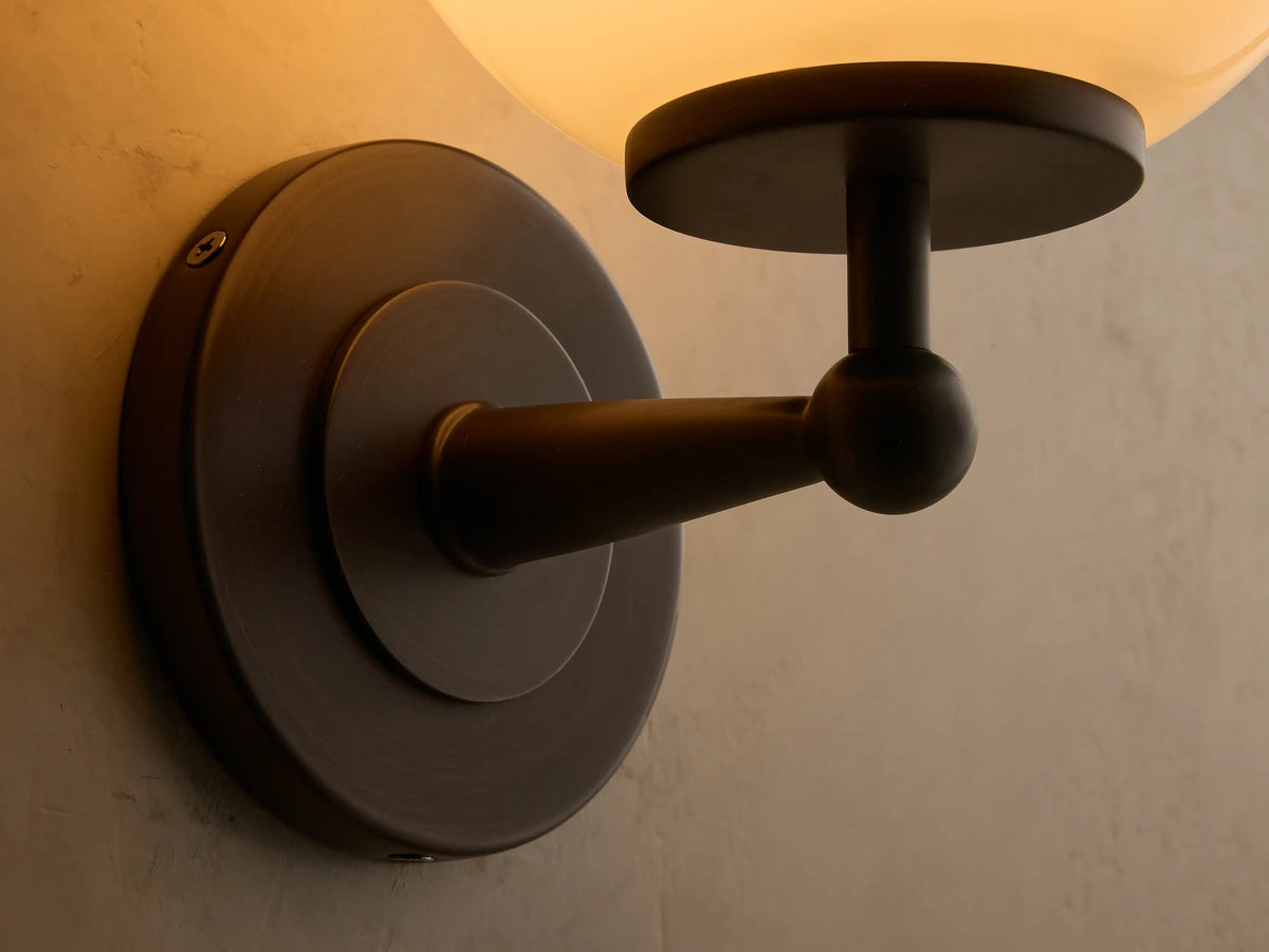 Close-up of the Fulton sconce antique bronze backplate and glowing milk glass globe