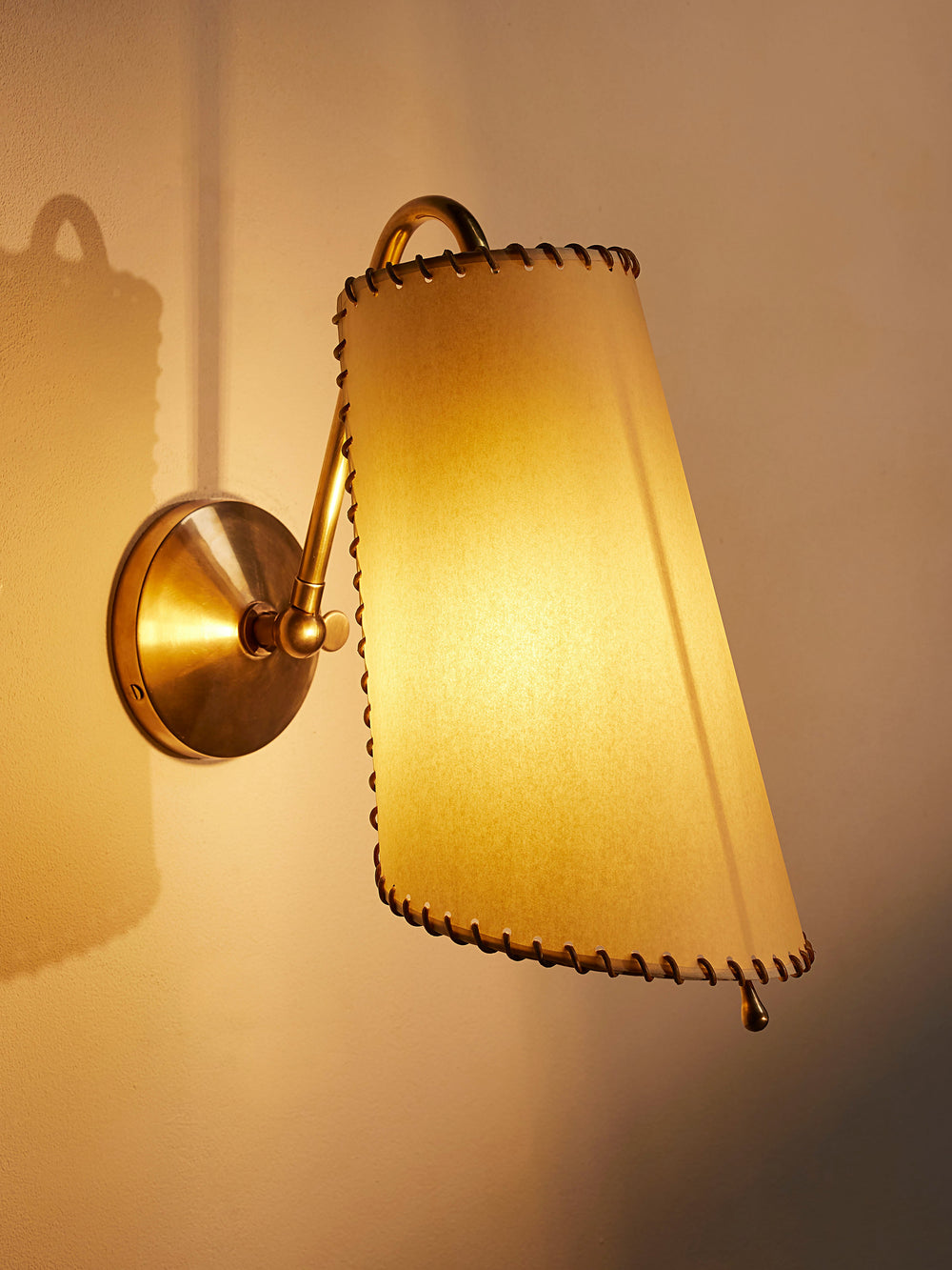 Zachary wall light illuminated, showing the antique-brass arm and leather-trimmed shade