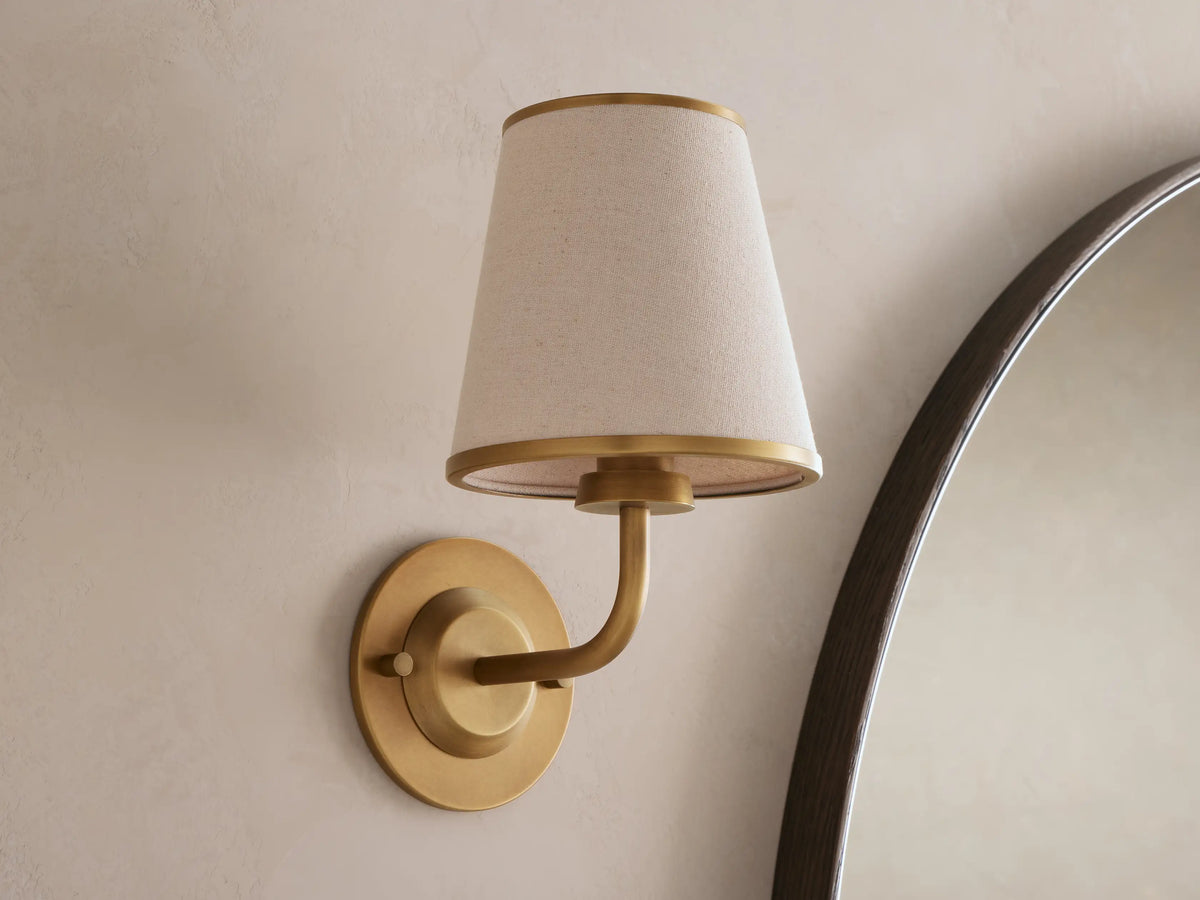 Adria Flax Sconce with brass-finished arm and fabric shade beside a mirror