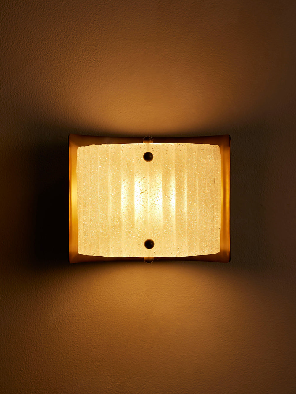 Bronte wall sconce illuminated, front view of frosted ribbed glass
