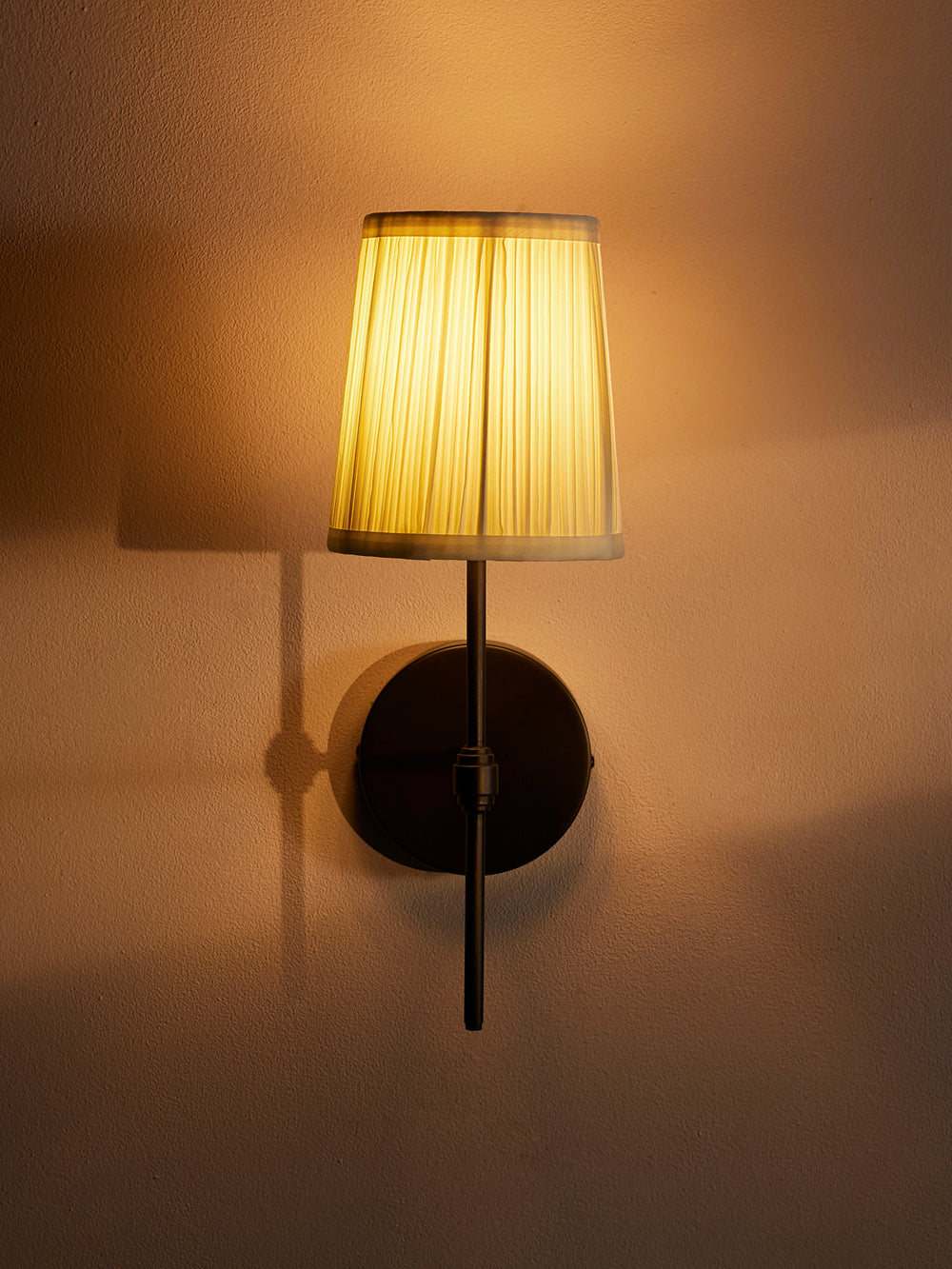 Isobella wall sconce illuminated with ivory pleated cotton shade and blackened brass frame