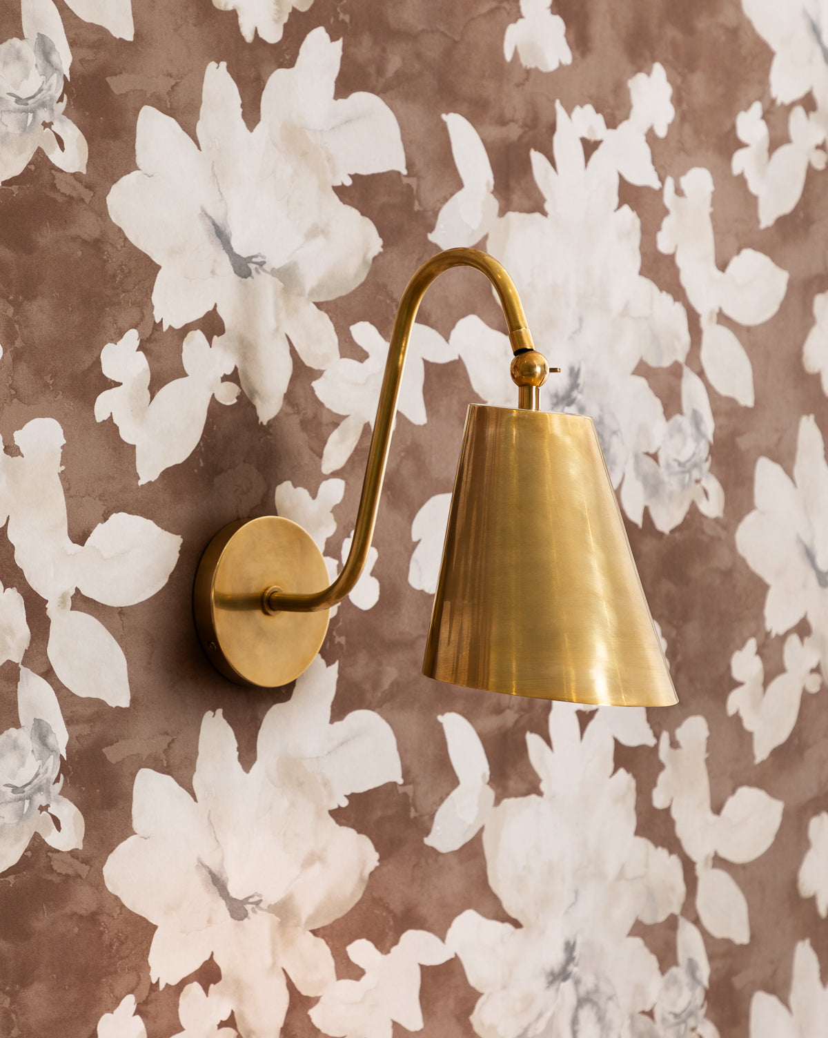 Saylor antique brass wall sconce installed against floral wallpaper